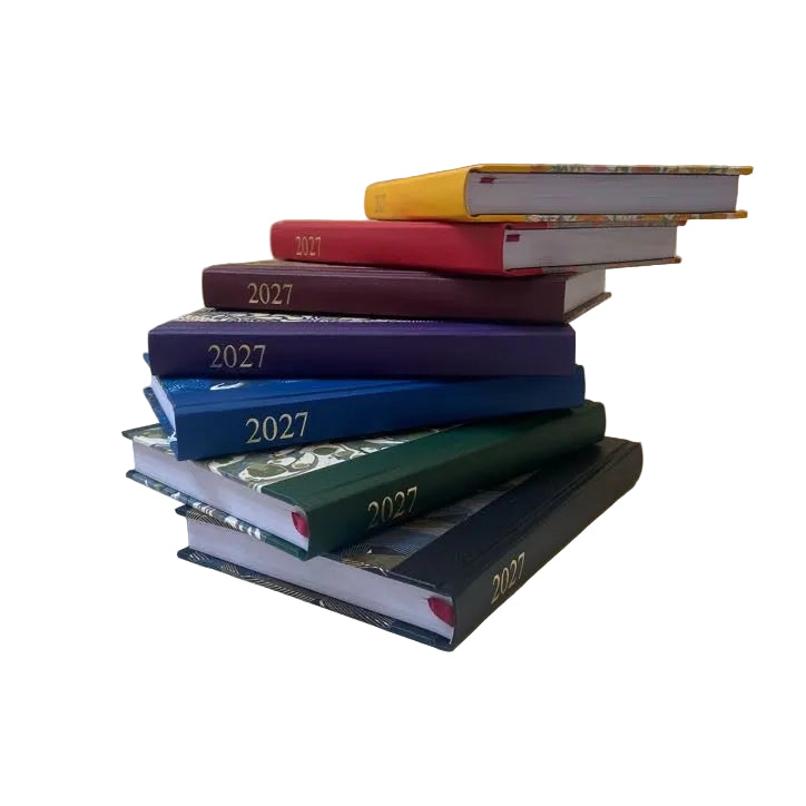 A stack of six hardcover 2027 books or journals in different colors including yellow, red, purple, blue, green, and black, arranged on a light beige paper backdrop.