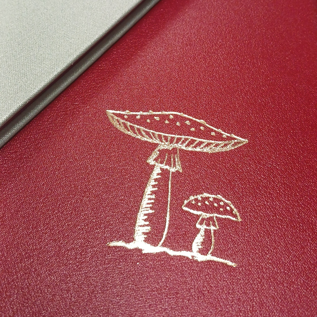 Red leather-look notebook with gold mushroom illustration