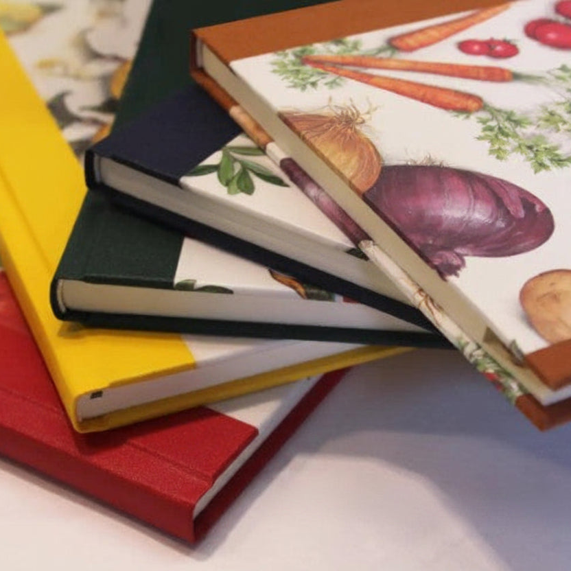 Stack of cookbooks with colorful covers featuring illustrations of vegetables on a white surface.